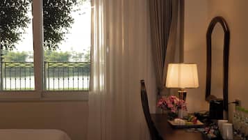 Habitación de hotel con cama, escritorio con lámpara, espejo y vista a un lago a través de una ventana con cortinas.