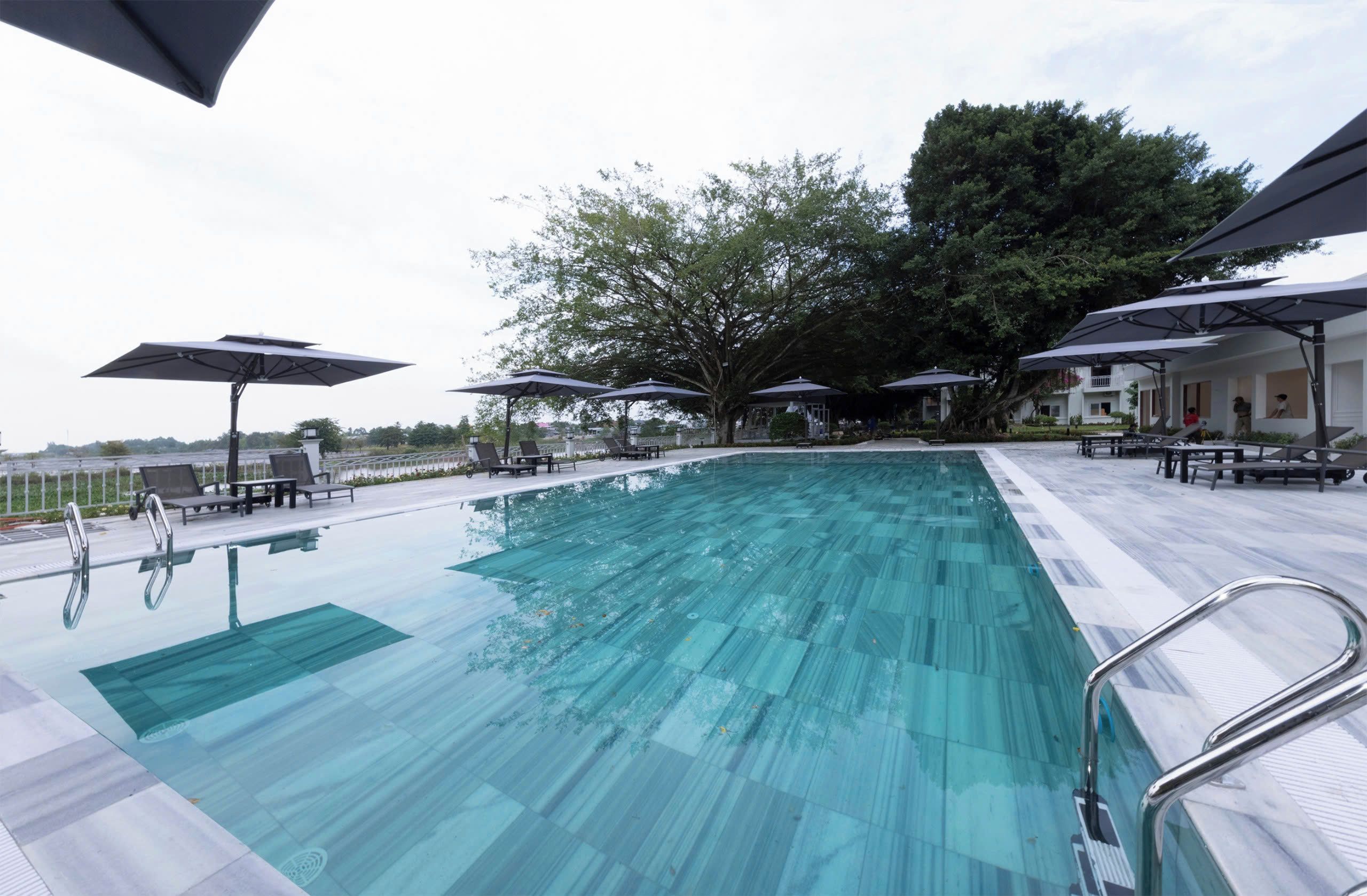 A swimming pool with lounge chairs and umbrellas, surrounded by trees and a building.