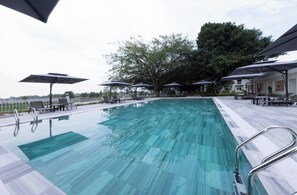 A swimming pool with lounge chairs and umbrellas, surrounded by trees and a building. - Merperle Núi Sam Resort (Vinh Te)