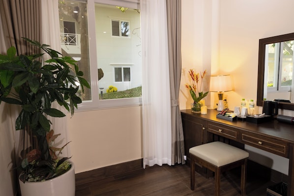 Een hotelkamer met een houten bureau, een stoel, een kamerplant, een lamp en een raam met gordijnen.