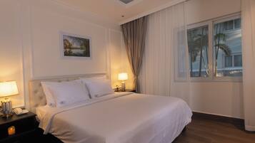 A hotel room with a large bed, a nightstand with a lamp, a framed picture on the wall, and a window with curtains.
