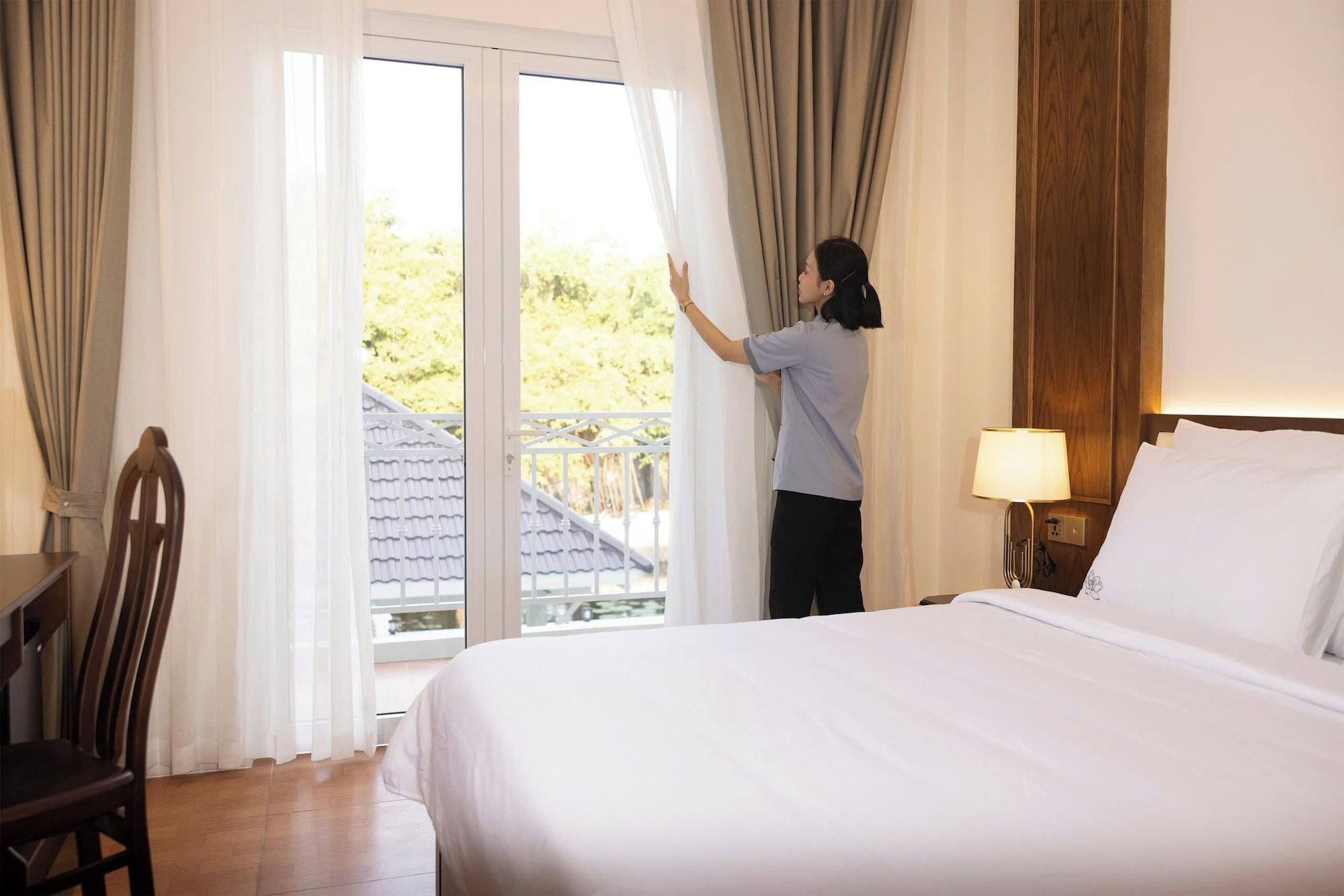 A hotel room with a bed, a nightstand with a lamp, and a view of a balcony with curtains.