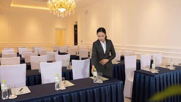 Un salón de conferencias con mesas dispuestas para una reunión, cada una con botellas de agua y vasos.