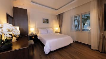 A hotel room with a large bed, a desk with a lamp, a mirror, and a window with curtains.