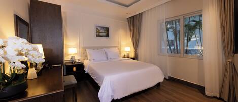 A hotel room with a large bed, bedside lamps, a nightstand, a mirror, and a window with curtains.