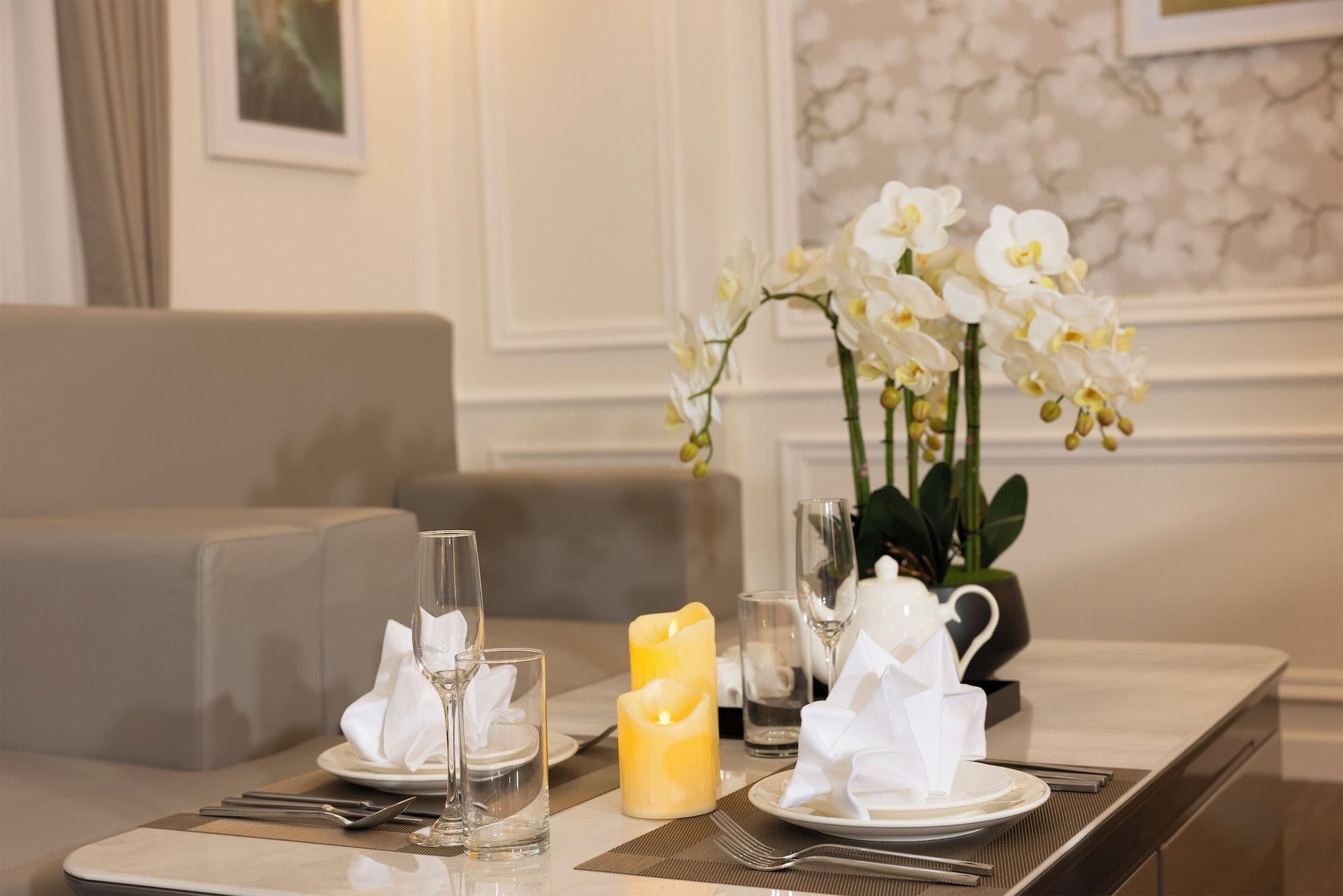 Una mesa de comedor dispuesta con platos blancos, servilletas, copas, velas y un jarrón con orquídeas blancas.