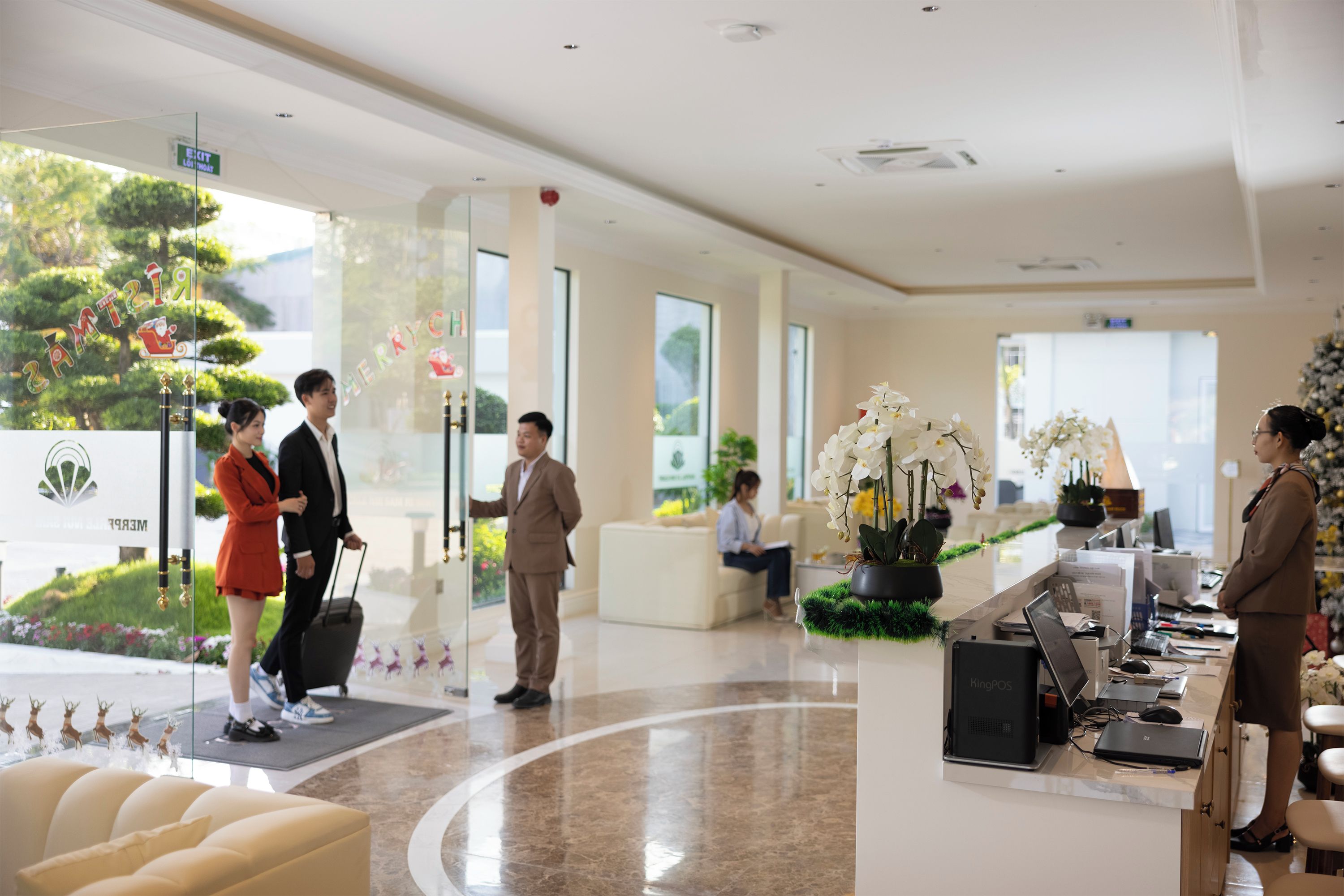 A hotel lobby with a reception desk, seating area, and a view of greenery outside.