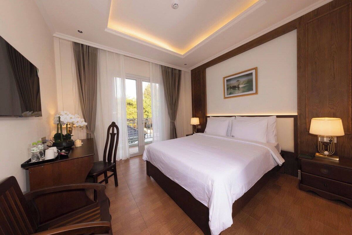 A hotel room with a large bed, a desk with a chair, a nightstand, and a picture on the wall.