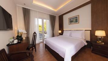 Habitación de hotel con una cama grande, un escritorio con silla, una mesita de noche y un cuadro en la pared.