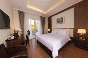A hotel room with a large bed, a desk with a chair, a nightstand, and a picture on the wall. - Merperle Núi Sam Resort (Vinh Te)