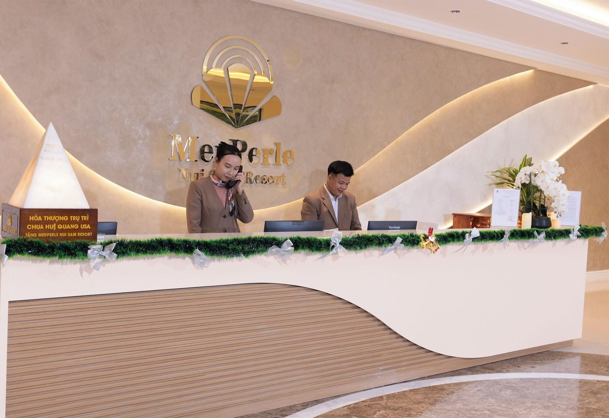 A reception desk at MerPerle NUI SAM Resort with a modern design, including a logo above the desk and a nameplate.