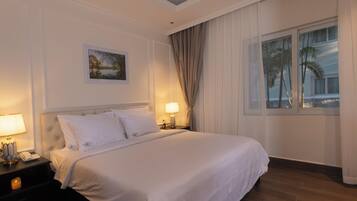 A hotel room with a large bed, two bedside lamps, a nightstand, a painting on the wall, and a window with curtains.
