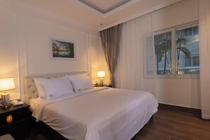 Een hotelkamer met een groot bed, twee bedlampjes, een nachtkastje, een schilderij aan de muur en een raam met gordijnen.