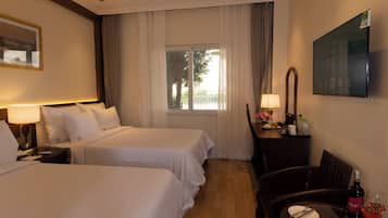 A hotel room with two beds, a desk with a chair, a TV, and a window with curtains.