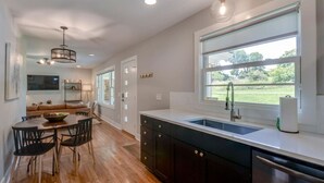 Une cuisine moderne dotée d’une grande fenêtre, d’un plancher en bois et d’un coin repas avec une table et des chaises.
