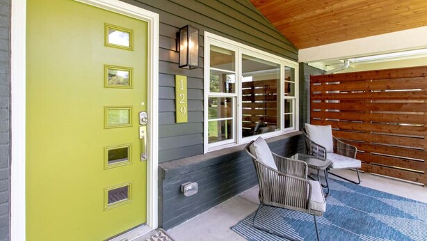 Une maison avec une porte verte, une véranda avec deux fauteuils en osier et une clôture en bois.