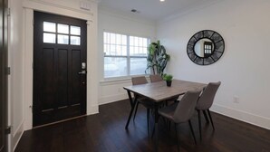 A dining area with a dark wooden table and chairs, a potted plant, and a wall-mounted fan.