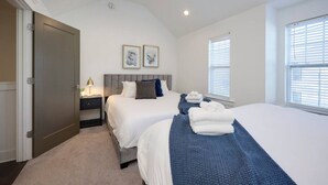 A bedroom with two beds, a nightstand, a lamp, and artwork on the wall.