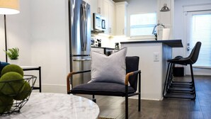 A modern kitchen with a stainless steel refrigerator, a dining area with a marble table, and a seating area with a cushioned chair.