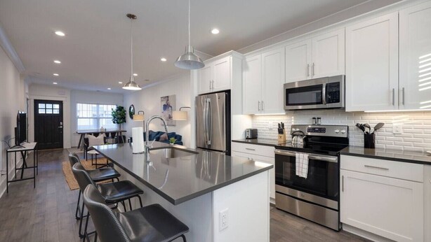 A modern kitchen with white cabinets, stainless steel appliances, a central island with bar stools, and pendant lighting.