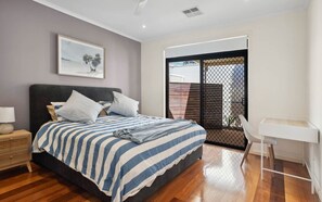 A bedroom with a bed, a nightstand, a chair, and a window with blinds. - Chiton Rocks Court! Mini Oasis by the Sea (Chiton)