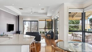 Una cocina moderna con una isla central, un área de comedor con una mesa de vidrio y una sala de estar con sofá y sillones.