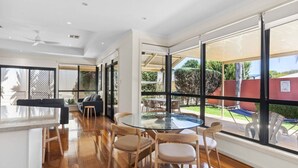 Amplia sala de estar con mesa y sillas de vidrio, ventanas grandes que ofrecen vistas al exterior y un ventilador de techo.