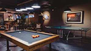 Uma mesa de bilhar com bolas, uma mesa de pingue-pongue e um letreiro de neon indicando estacionamento.