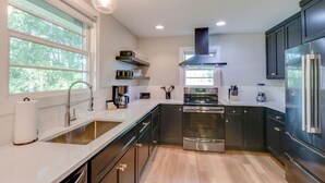 A modern kitchen with dark cabinetry, a stainless steel oven, and a large window providing natural light. - Cute And Cozy - Historic Franklin Quadplex (Franklin)