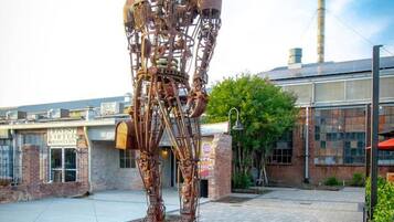 A large metal sculpture of a human figure in an outdoor plaza with brick pathways and greenery.