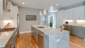 Une cuisine moderne dotée d’un îlot en marbre, d’appareils électroménagers en acier inoxydable et de luminaires suspendus.