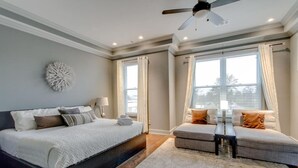 Une chambre à coucher avec un grand lit, un canapé, un ventilateur de plafond et de grandes fenêtres avec des rideaux.