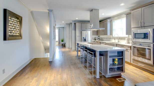Une cuisine moderne dotée d’un îlot central, d’appareils électroménagers en acier inoxydable et d’un plancher en bois.