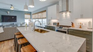 Une cuisine moderne dotée d’un grand îlot central, d’appareils électroménagers en acier inoxydable et de luminaires suspendus.