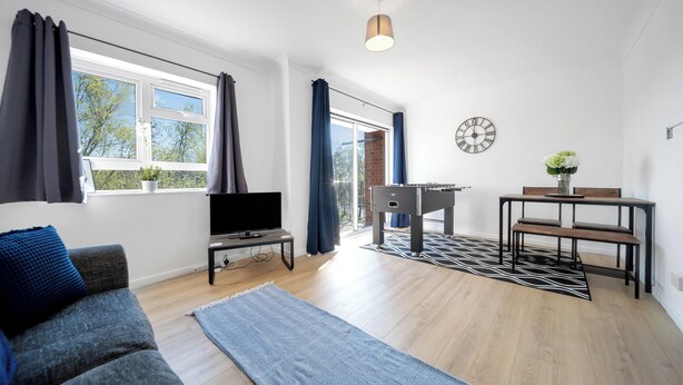 A modern living room with a sofa, TV, dining table, and a view of the outdoors.