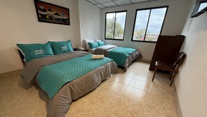 A hotel room with two beds, teal bedding, a painting on the wall, and a view through the windows. - Hotel Suite Centro Bogota (Bogotá)