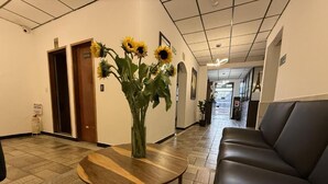 A lobby with a round wooden table, a black leather couch, and a vase with sunflowers. - Hotel Suite Centro Bogota (Bogotá)