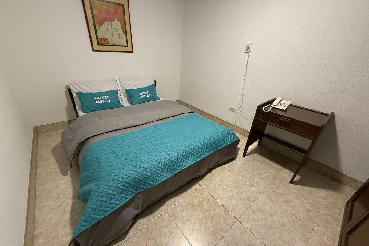 A hotel room with a bed, a desk, and a telephone.