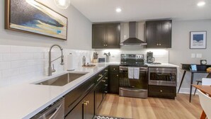 A modern kitchen with a double sink, stainless steel appliances, dark cabinetry, and a painting above the sink. - Spacious & Peaceful-  Historic Franklin Quadplex (Franklin)