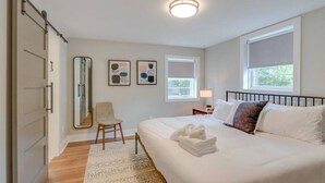 A bedroom with a bed, a chair, a nightstand, a lamp, a window, and a mirror. - Spacious & Peaceful-  Historic Franklin Quadplex (Franklin)