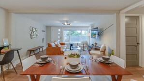 A dining area with a wooden table set for four, a sofa, and a TV mounted on the wall. - Spacious & Peaceful-  Historic Franklin Quadplex (Franklin)