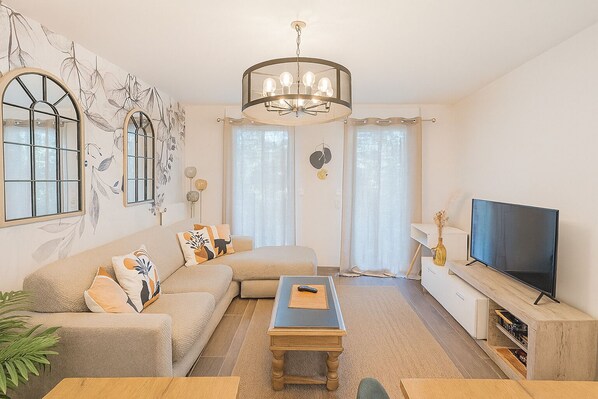 A modern living room with a sectional sofa, a wooden coffee table, a flat-screen TV, and a chandelier. - Le Plessis-Capitale: Apartment with a private garden (Le Plessis-Robinson)