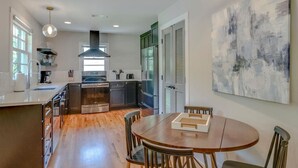 A modern kitchen with a central island, wooden flooring, and a dining area with a round table and chairs. - Pretty & Bright - Historic Franklin Quadplex (Franklin)