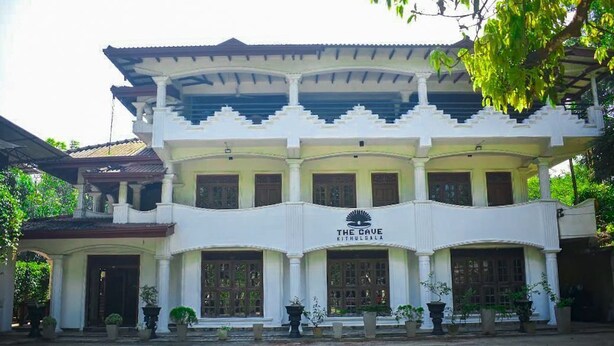A two-story building with a sign reading "The Cave Kithoolala." It features a symmetrical facade with columns, large windows, and a covered entrance area. - The Cave Kithulgala (Kithulgala)