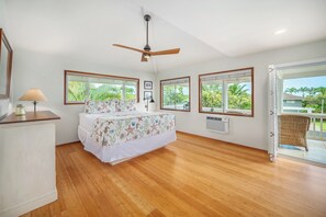 A bedroom with a bed, a ceiling fan, a window, and a door leading to a balcony.