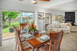 A dining area with a table set for four, surrounded by wooden chairs. There is a sofa and a fireplace in the background.