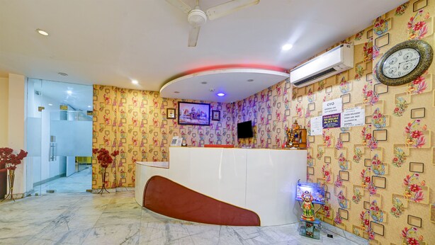 Un hall d’hôtel avec un comptoir d’accueil incurvé, un ventilateur de plafond, un téléviseur fixé au mur et une horloge sur le mur.