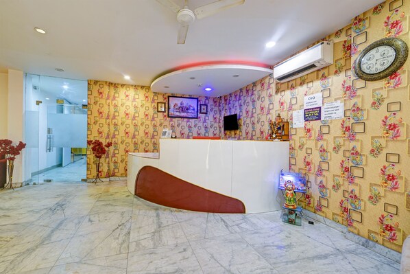 Zona de recepción de hotel con un mostrador curvo, un ventilador de techo, un televisor montado y un reloj en la pared.