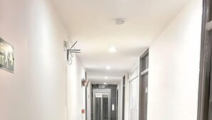 Un long couloir étroit aux murs blancs et au sol carrelé brillant, qui mène à une pièce dont la porte se trouve au fond.