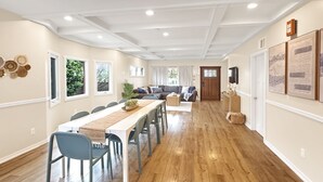 A spacious living room with a long dining table, a sofa, and a TV mounted on the wall.